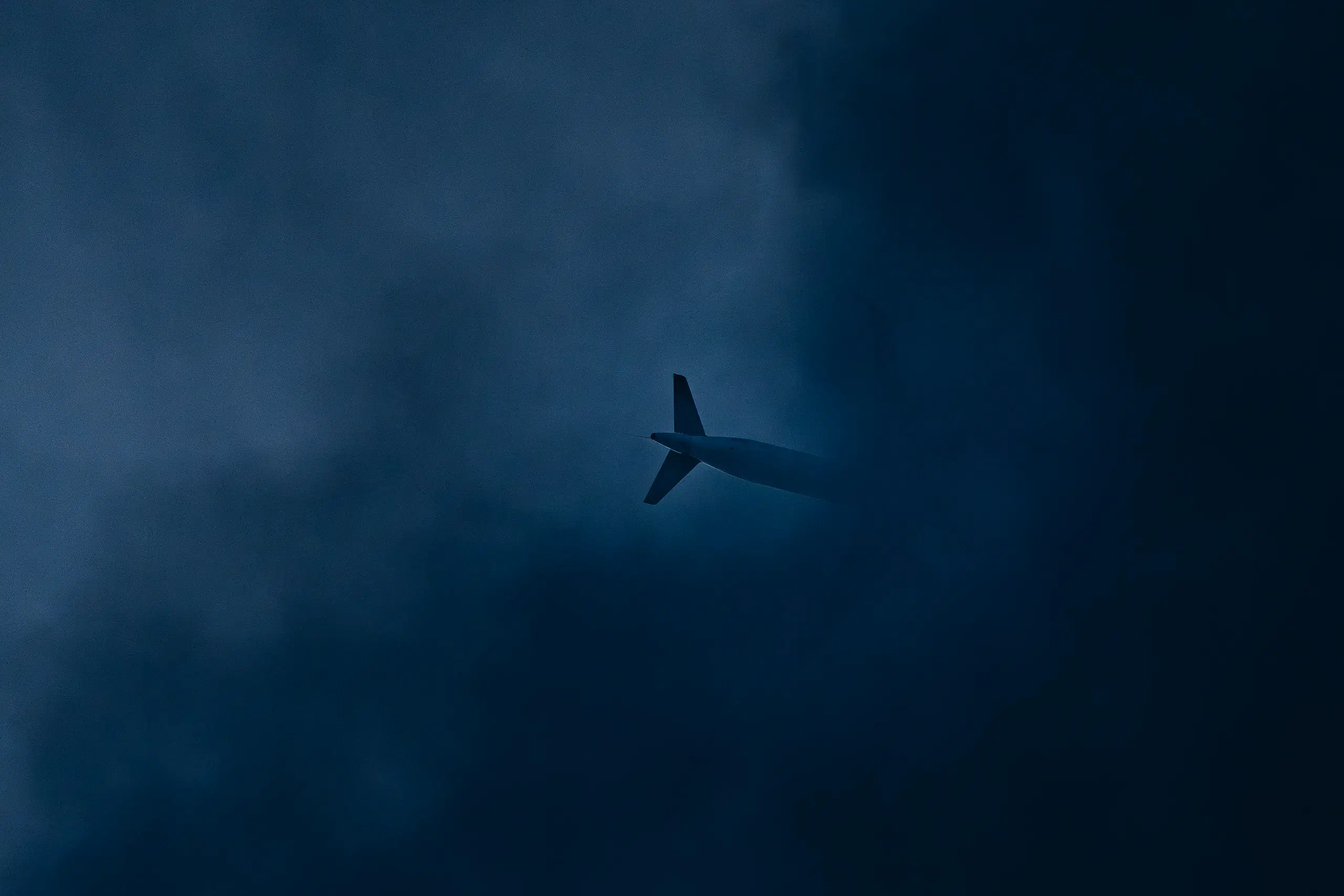A distant airliner crossing a deep blue-grey sky, half dissolved into heavy cloud.